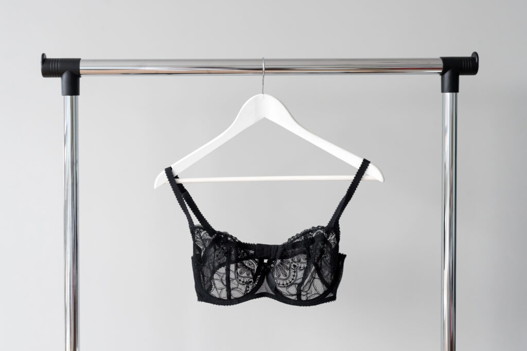 black-lace-bra-on-white-hanger-against-neutral-background » milwaukeelingerie.com Black lace bra on a white hanger, styled on a chrome rack—minimalist image for a Milwaukee lingerie and bra fitting guide.